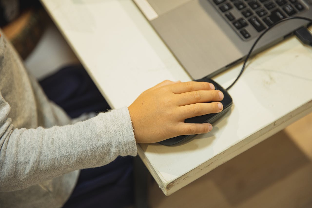 Close-up of a child's hand using a laptop and mouse for online learning indoors.