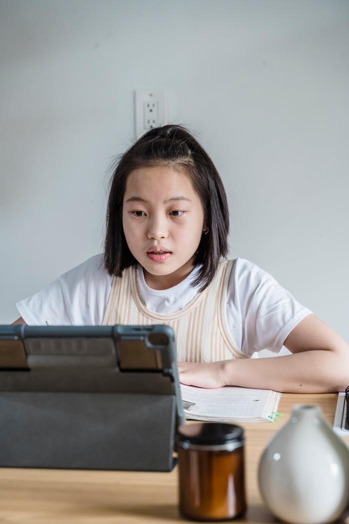 Asian girl focusing on online class using a tablet in a home setting, engaged in learning.